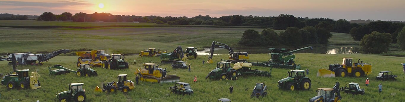 Ljudi koji hodaju između nekoliko vrsta opreme John Deere na velikom polju.