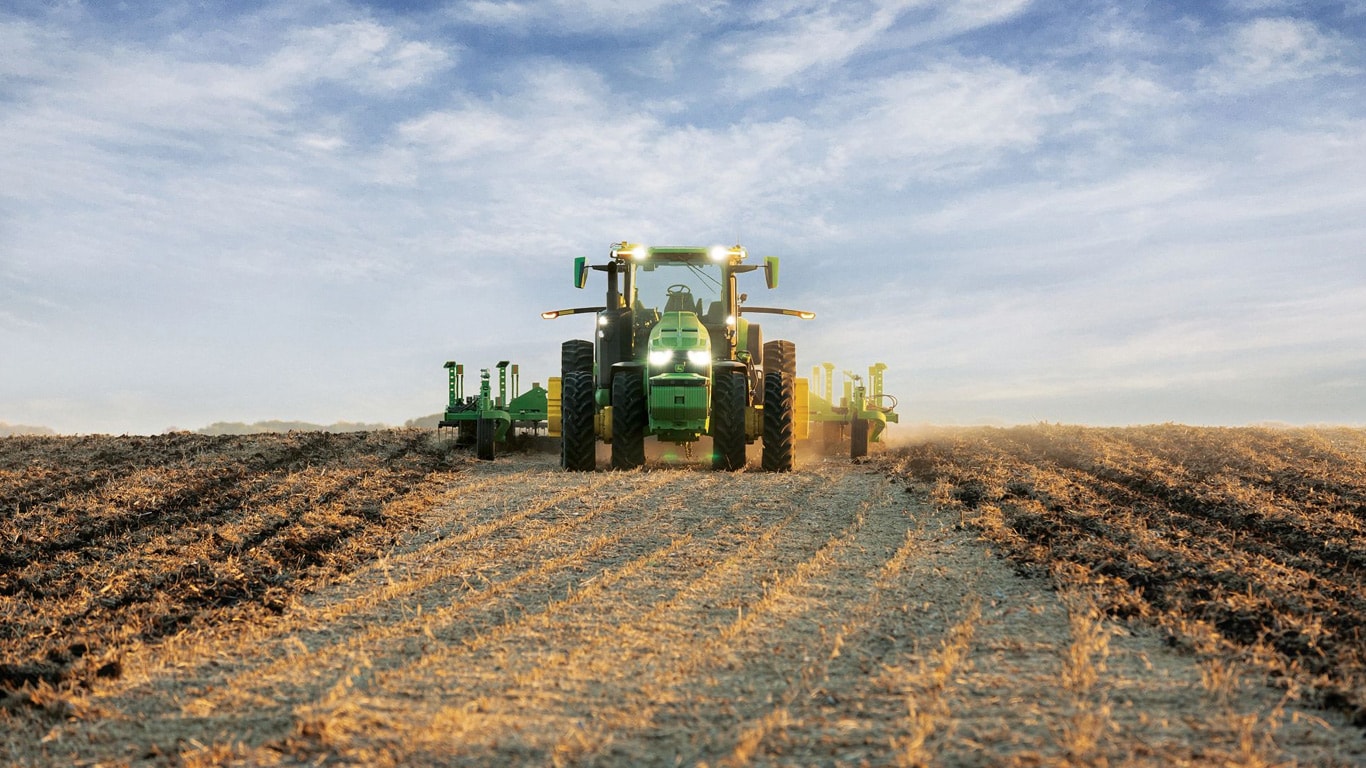 Samohodni traktor tvrtke John Deere vuče opremu za prevrtanje kroz otvoreno polje.