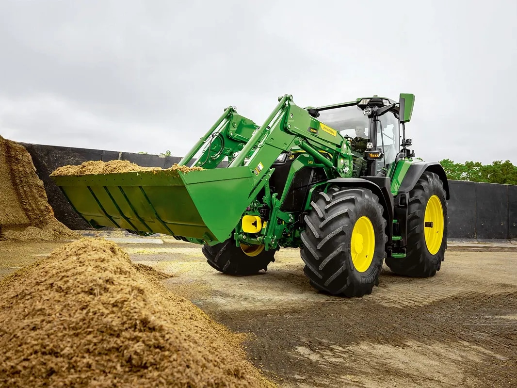 Žlica prednjeg utovarivača napunjena silažom na traktoru John Deere tijekom rukovanja materijalom.