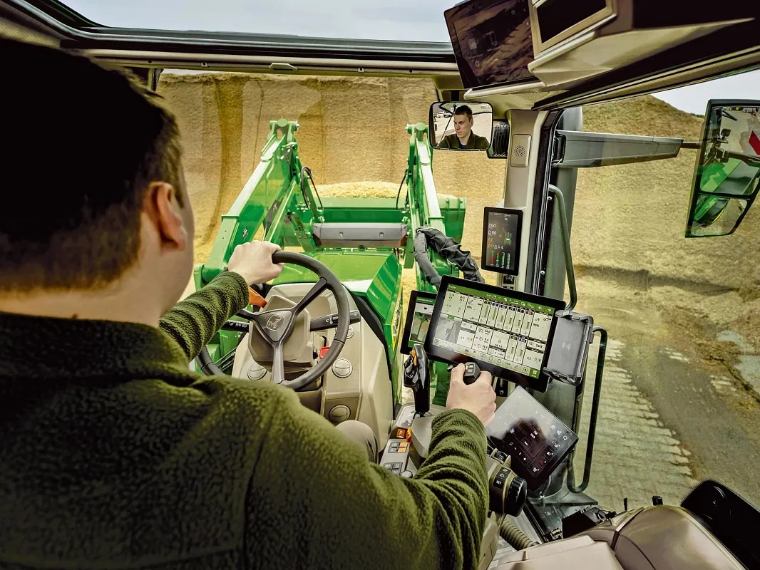 Pogled u unutrašnjost kabine traktora John Deere s prikazanim upravljačkim elementima rukovatelja i radom prednjeg utovarivača.