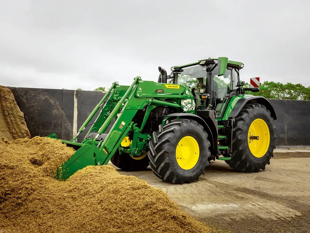 Traktor John Deere žlicom prednjeg utovarivača potiskuje hrpu silaže u okruženju farme.