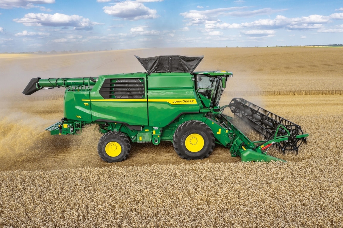 Bočni pogled na John Deere kombajn s reznim hederom koji žanje pšenicu u velikom poljoprivrednom polju