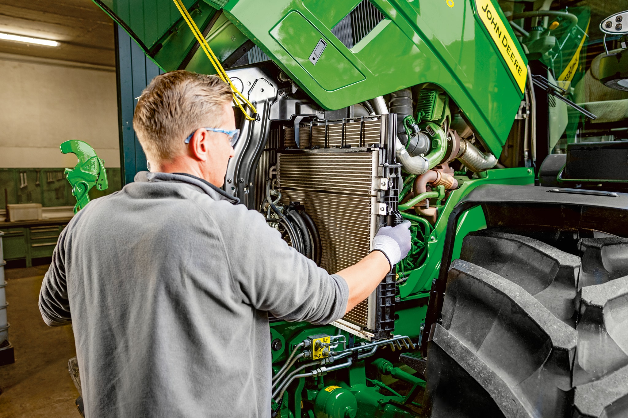 Servisni tehničar koji provodi održavanje u motornom prostoru traktora John Deere serije 6M.
