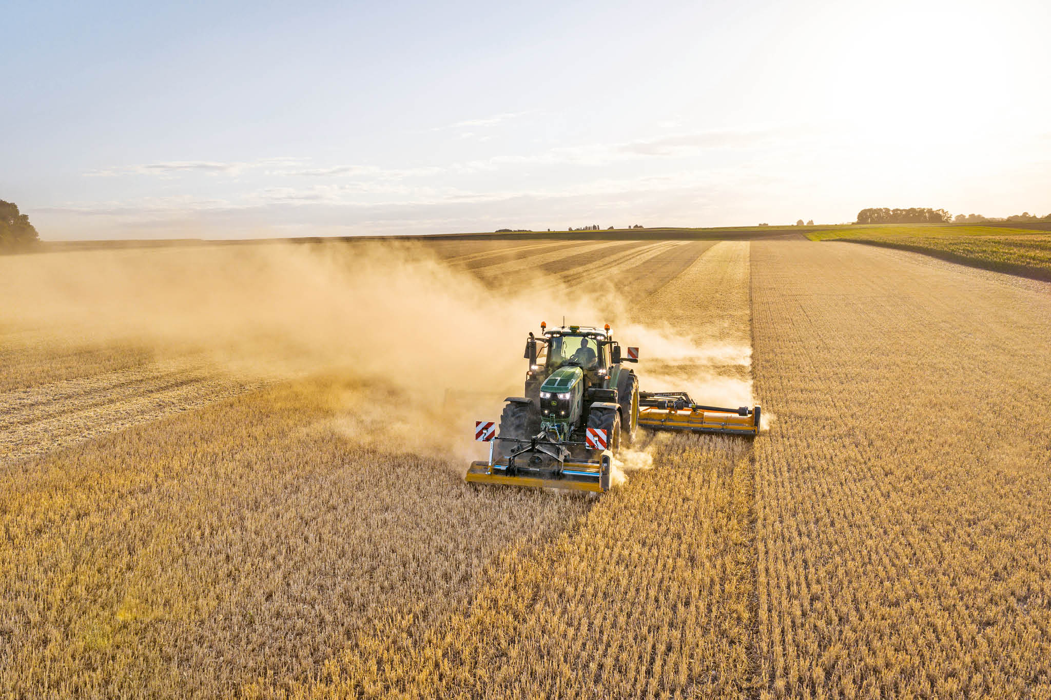 Traktor John Deere serije 6M vuče cisternu tekućeg gnojiva po ruralnoj cesti kroz pašnjake i polja.