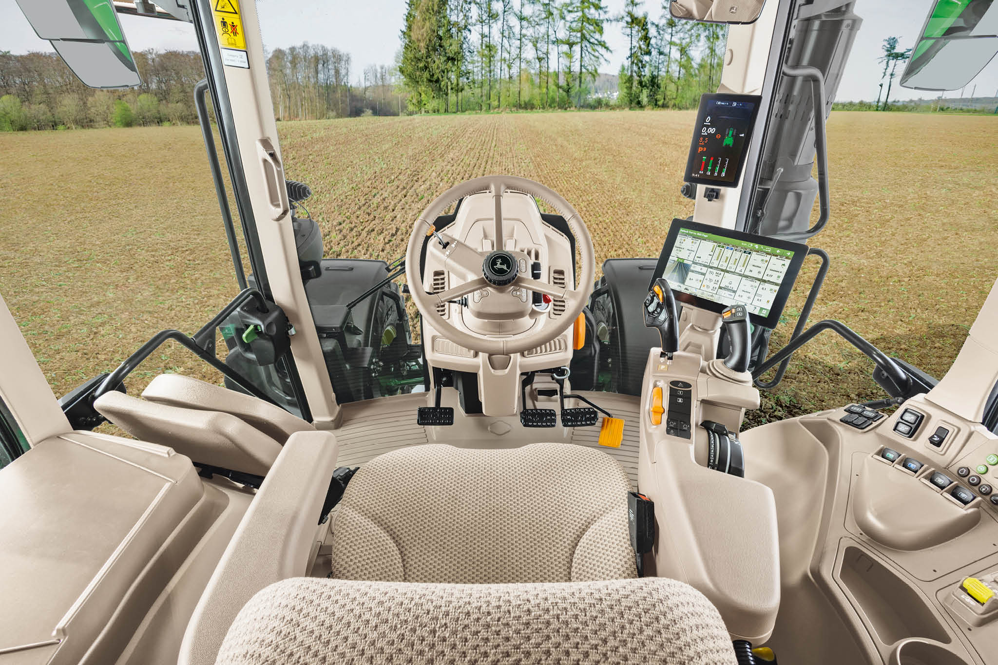 Pregled unutrašnjosti kabine traktora John Deere serije 6M sa sjedalom vozača, kolom upravljača i digitalnim zaslonima.