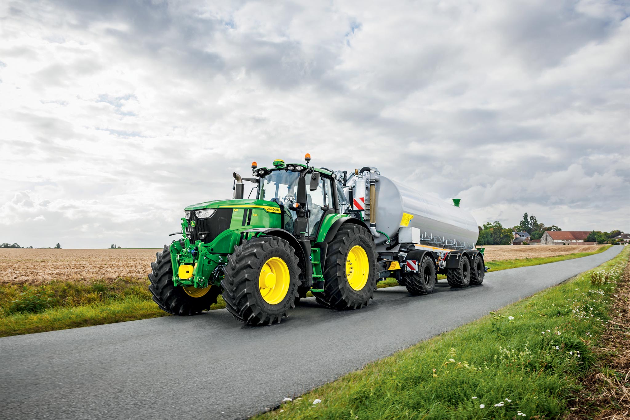 Traktor John Deere serije 6M radi na požetom polju sa širokim kultivatorima, gledano odozgo s prašinom koja se podiže.