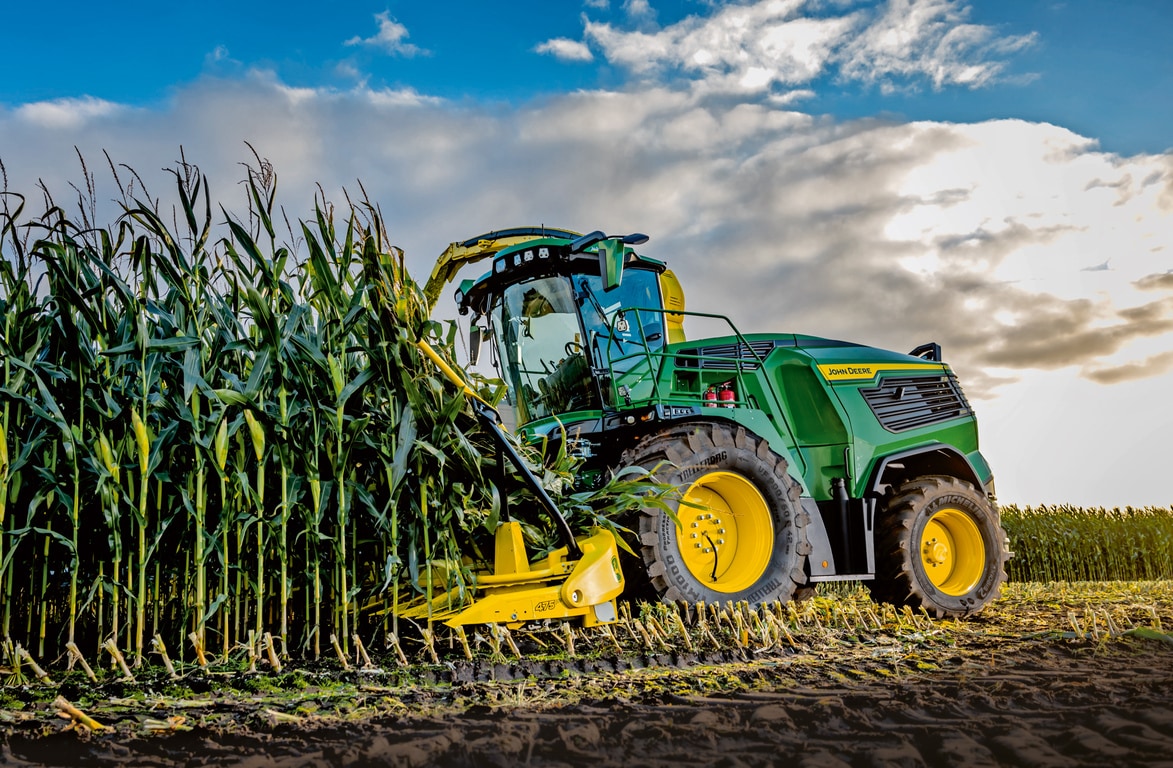 John Deere sakuplja kukuruz u polju pod plavim nebom s oblacima.