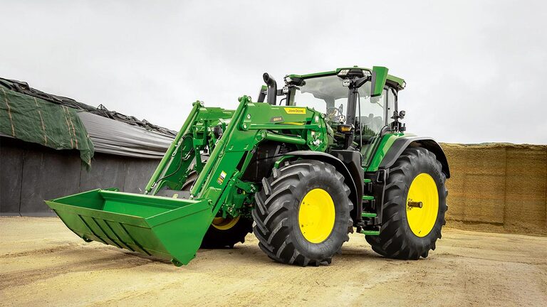 Traktor John Deere s prednjim utovarivačem parkiran na farmi blizini skladišta silaže.