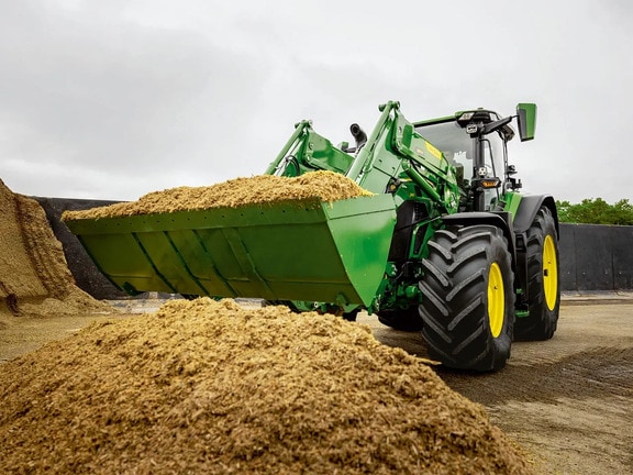 Traktor John Deere prednjim utovarivačem prevozi usitnjenu silažu u prostoru za skladištenje poljoprivrednih proizvoda.