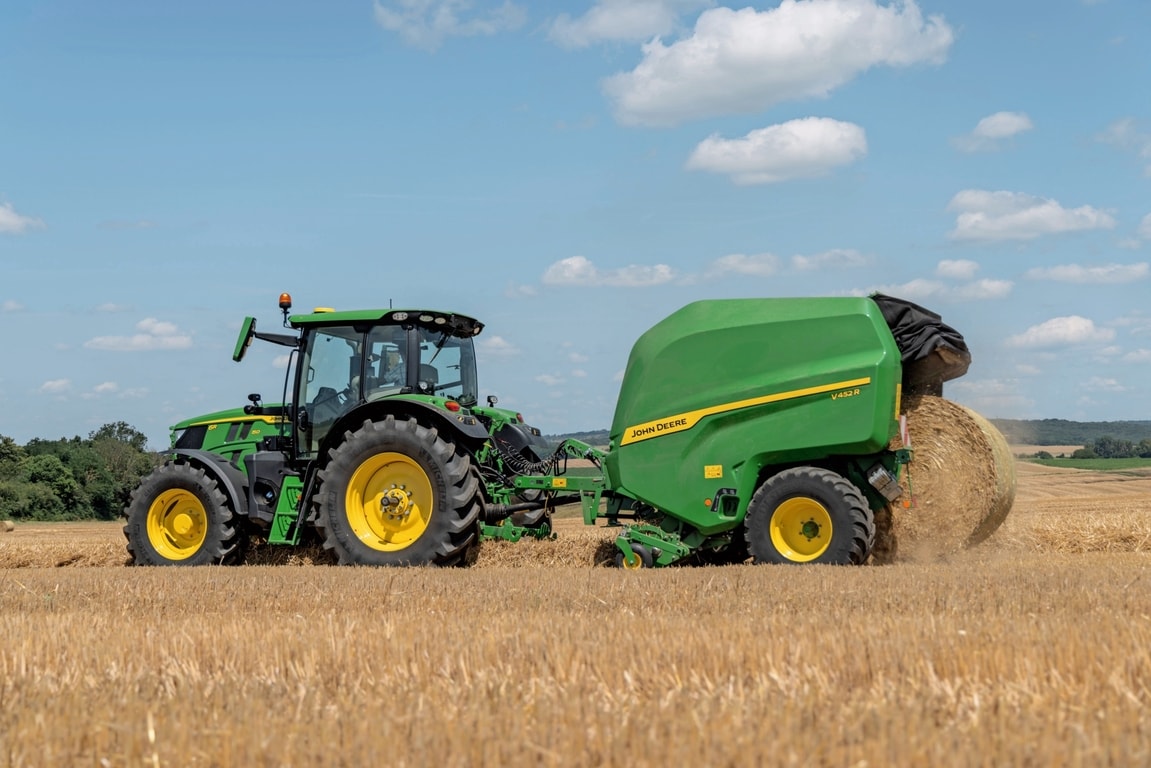 John Deere V452R na polju slame koje vuče John Deere 6R 150 izbacujući balu