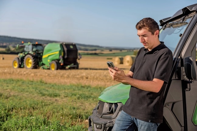 Osoba koja provjerava podatke dokumentacije bale na mobilnom telefonu s John Deere VR balirkom u pozadini
