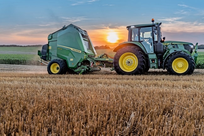 John Deere V462M na polju slame kojeg vuče John Deere 6M 150 u zalazak sunca