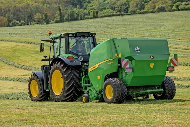 John Deere F442M balirka koju vuče traktor John Deere 6M na brdovitom travnatom polju