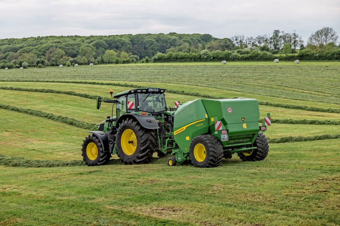 John Deere F442R balirka koju vuče traktor John Deere 6M na brdovitom travnatom polju
